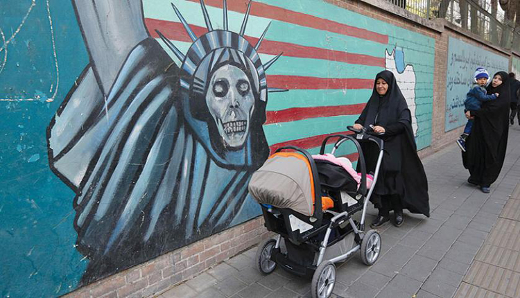 أمرأة إيرانية تمشي بجانب جدارية فيها صورة تمثال الحرية على شكل جمجمة 