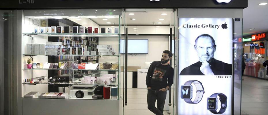 بائع يقف أمام محل بيع الأجهزة الألكترونية وتظهر صورة شركة أمريكية 